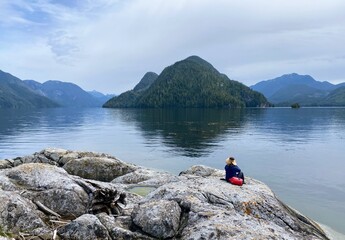 A woman sits on a rocky island, admiring the stunning views of the Broughton Islands in the serene Broughton Archipelago.