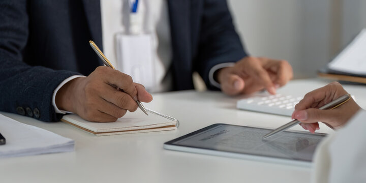 Professional Meeting. Hands of businessman and client writing notes and discussing finances.