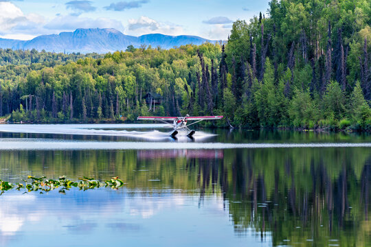 Small floatplane landing on the lake surrounded by the forest. High mountains as the background