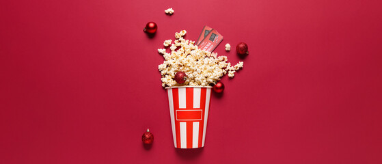 Bucket of popcorn with cinema tickets and Christmas tree balls on red background