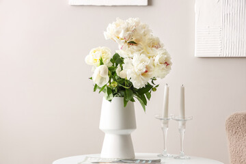 Vase of white peonies with candles and magazine on coffee table near wall
