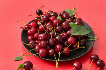 Plate with sweet cherries on red background