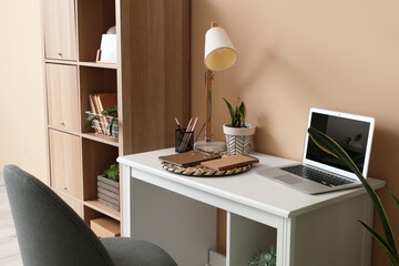 Comfortable workplace with modern laptop and lamp near color wall
