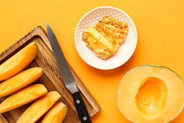 Wooden board with pieces of sweet melon on orange background