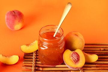 Jar with sweet peach jam and fresh fruits on orange background