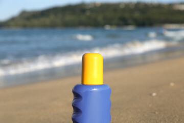 Bottle of sunscreen cream on sand near ocean at beach