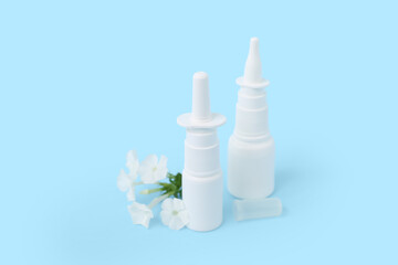 Bottles of nasal drops with flowers on blue background
