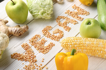 Word VEGAN made of dried peas and different fresh vegetables on white wooden background