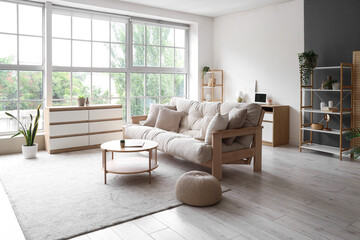 Interior of light living room with beige couch, table and big window
