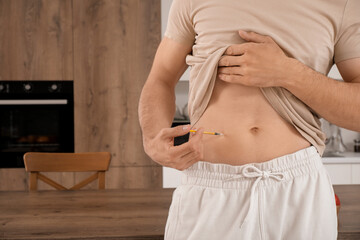 Diabetic young man giving himself insulin injection in kitchen, closeup