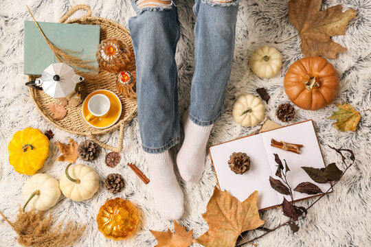 Female legs in warm socks with books, autumn leaves and pumpkins on white plaid as background