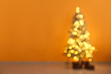 Blurred view of decorated Christmas tree with glowing lights and gift boxes near yellow wall