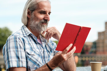 Senior man enjoying a book outdoors in urban setting