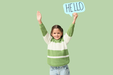 Cute little happy girl holding paper speech bubble with word HELLO while waving hand on green background