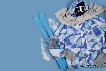 Winter clothes with skis and snow on blue background, top view