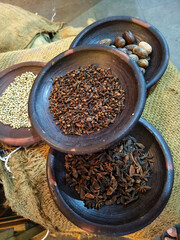 Assorted spices displayed in rustic wooden bowls, including cloves, star anise, nutmeg, and coriander seeds