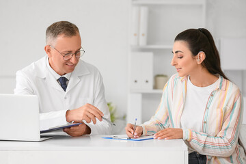 Obraz premium Young woman with hearing aid visiting doctor at table in clinic