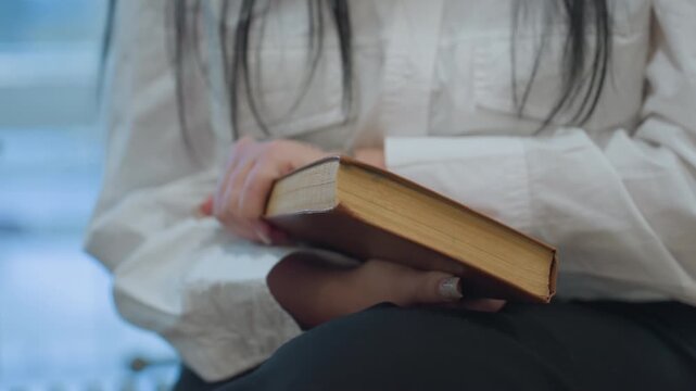 Close up on woman manicured nails gripping hardcover book then slamming it shut in frustration, stray pages trembling, blurred modern interior background