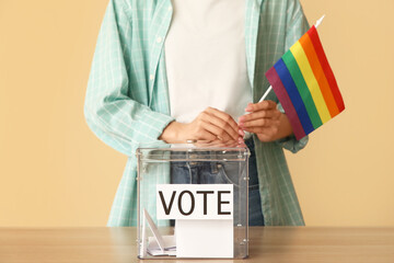Voting woman with LGBT flag near ballot box on beige background