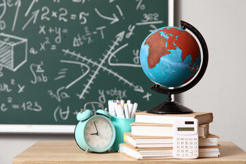 Globe with books, pen cup and alarm clock on desk in classroom