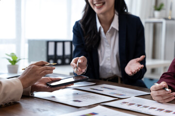 Colleagues in a modern office collaborate over charts, sharing a smartphone and discussing strategy...
