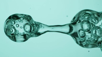 Merging Water Spheres Connected by a Thin Stream with Bubbles Under Cyan Background Eye Level Shot Perfect for Demonstrating Scientific Experiment or Conceptual Theme Close Up Video - Powered by Adobe