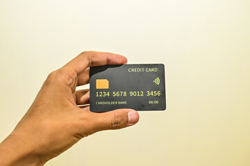 Hand holding black credit card isolated on beige or white background. Side. Close up. Wall. Light. Men, man, male. Asian. Budget. Earning.