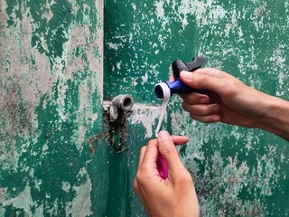Close-up of a hand applying pipe tape to a water faucet to prevent water from leaking from the connection between the faucet and the water pipe.