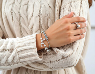 Elegant woman hand with pearl ring and silver bracelet on cozy cream cable knit sweater. gentle and warm fashion accessory detail