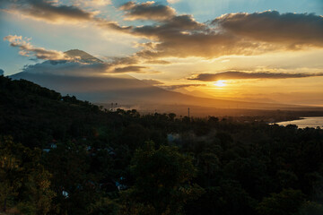 Scenic view from Amed, Bali – golden sunset light illuminating the ocean, tropical greenery and the silhouette of Mount Agung in the background.