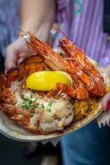 A plate of delicious, healthy, grilled lobster and prawns with a lemon wedge and paella.