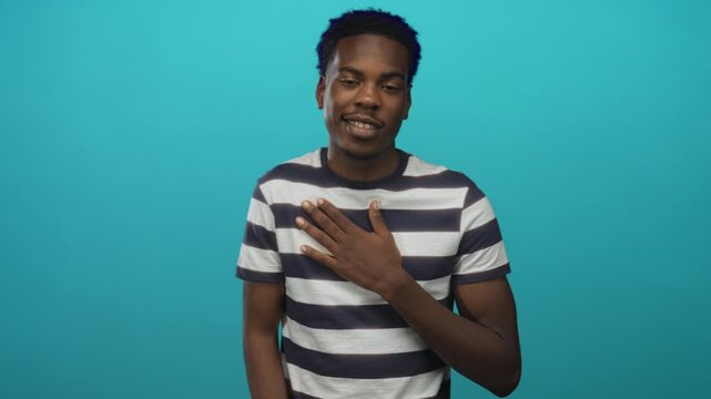 Young african american man with hand on chest gesture in teal studio; sincerity trust affirmation hope.