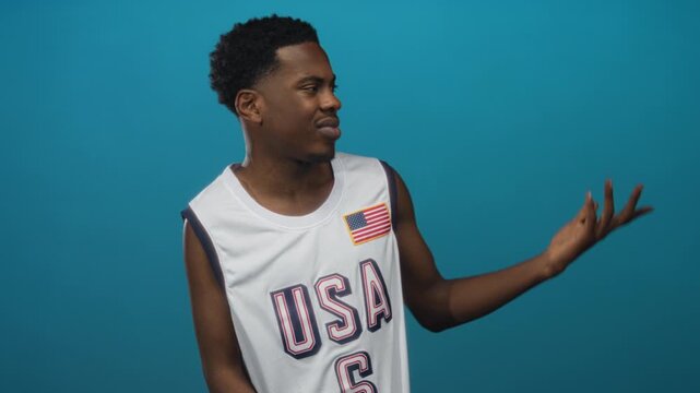 Man in white usa basketball jersey points finger at flag patch while smiling in teal studio; confidence.