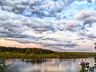 Beautiful landscape of a tranquil river surrounded by lush greenery and dramatic clouds during sunset