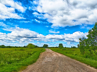 Beautiful rural dirt road stretches into the horizon under a vibrant blue sky filled with clouds © keleny