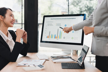 Quarterly business growth performance presentation with colleagues discussing colorful bar chart on desktop monitor, collaborative office meeting conveying professional focus and optimism