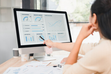 Woman pointing at desktop monitor displaying business analytics dashboard with charts and graphs, focused team collaboration and planning, productive office scene, soft natural light