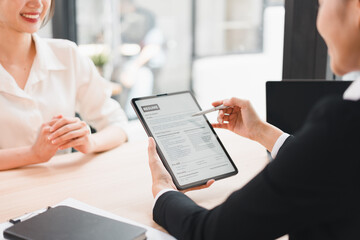 Young woman interview resume on tablet, recruiter pointing at qualifications, professional meeting, smiling candidate, office interior, candid interaction