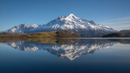 Fototapeta premium A serene natural landscape with a prominent snow capped mountain range reflected in calm water under a clear blue sky,