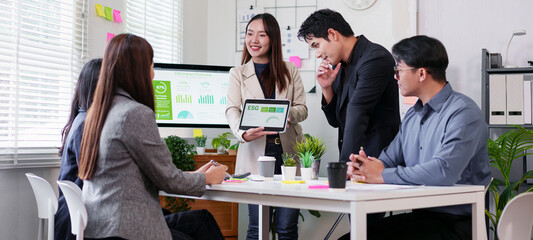 Young businesswoman presenting ESG report on tablet to diverse team in modern office, collaborative meeting with charts and plant on table showing sustainability focus and engaged discussion