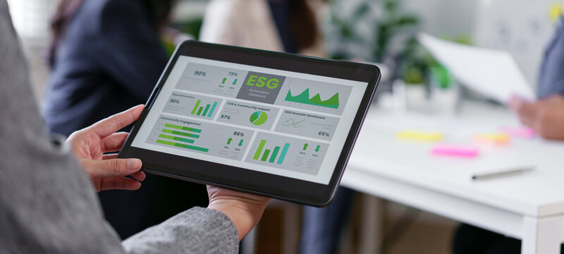 ESG performance dashboard on tablet displaying green charts and graphs, business team reviewing sustainability metrics in modern office, collaborative meeting with digital report - Powered by Adobe