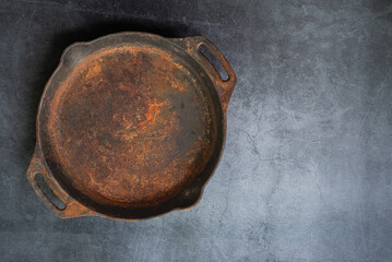 Old rusty round cast iron frying pan on grey cement background, view from above