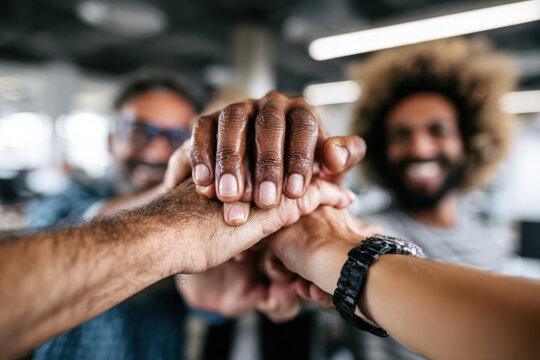 A group of coworkers stacking hands together in a modern office for teamwork spirit