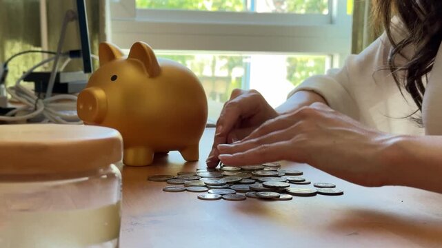The video footage shows the hand of a beautiful woman counting her coins and saving money in a piggy bank.