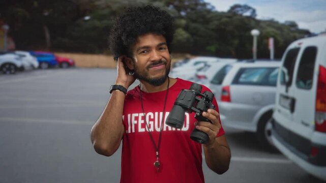 Man wearing lifeguard shirt holds binoculars on a busy city street with parked cars, showcasing an urban outdoor scene with a casual and relaxed vibe.