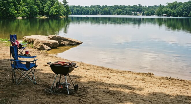 Barbecue grill and folding chairs on a sandy beach near a lake with an american flag on a chair