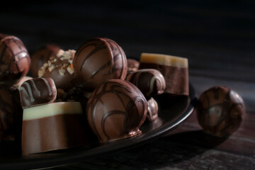 Assortment of chocolates on a dark plate and black background, chiaroscuro or Renaissance technique, Baroque style. Dark food macro photogrfaphy