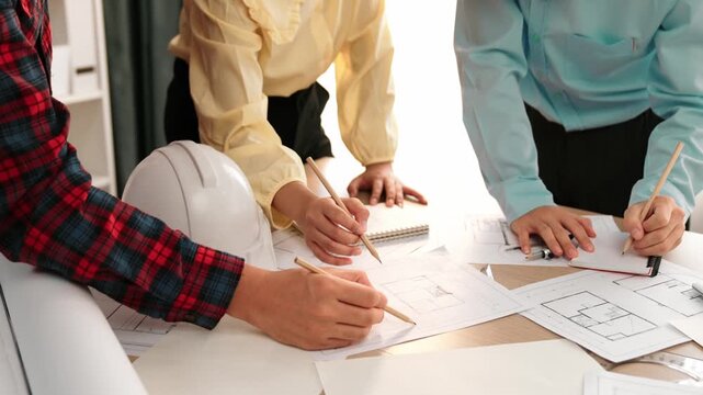 Smart architect and safety engineer discussion about building blueprint on table with architectural document, measurement tools and wooden block scatter around at modern office. Closeup. Delineation.