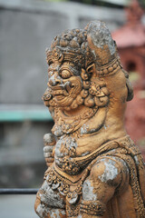 Ancient Balinese guardian statue. Close up of a traditional stone Dwarapala sculpture with intricate details and a weathered golden texture.
