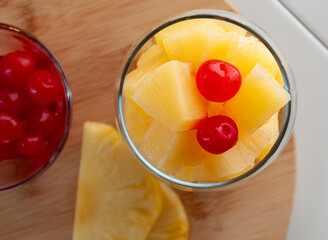 Pineapple fruit cocktail in a glass on a wooden cutting board with two cherries on top of the pineapple top view lay flat